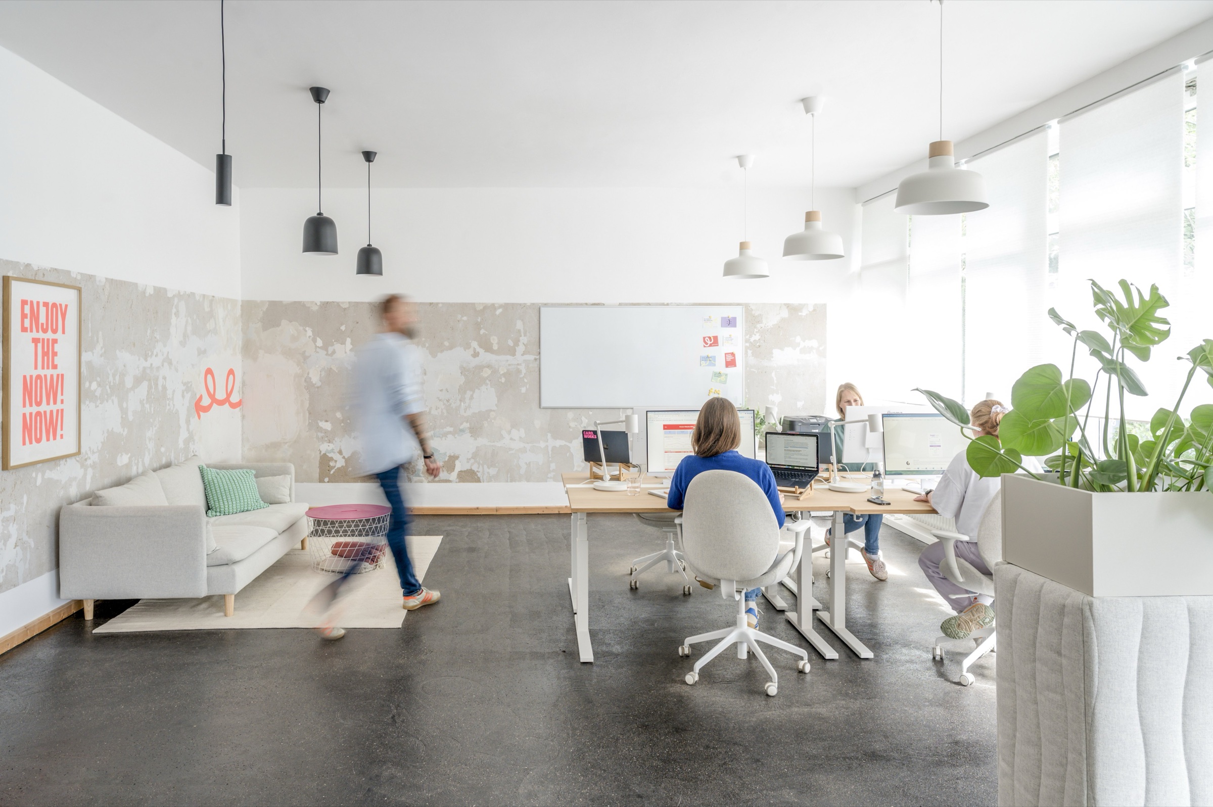 Helles, offenes Büro mit Schreibtischen, Sofa und Pflanzen, an denen mehrere Personen arbeiten.